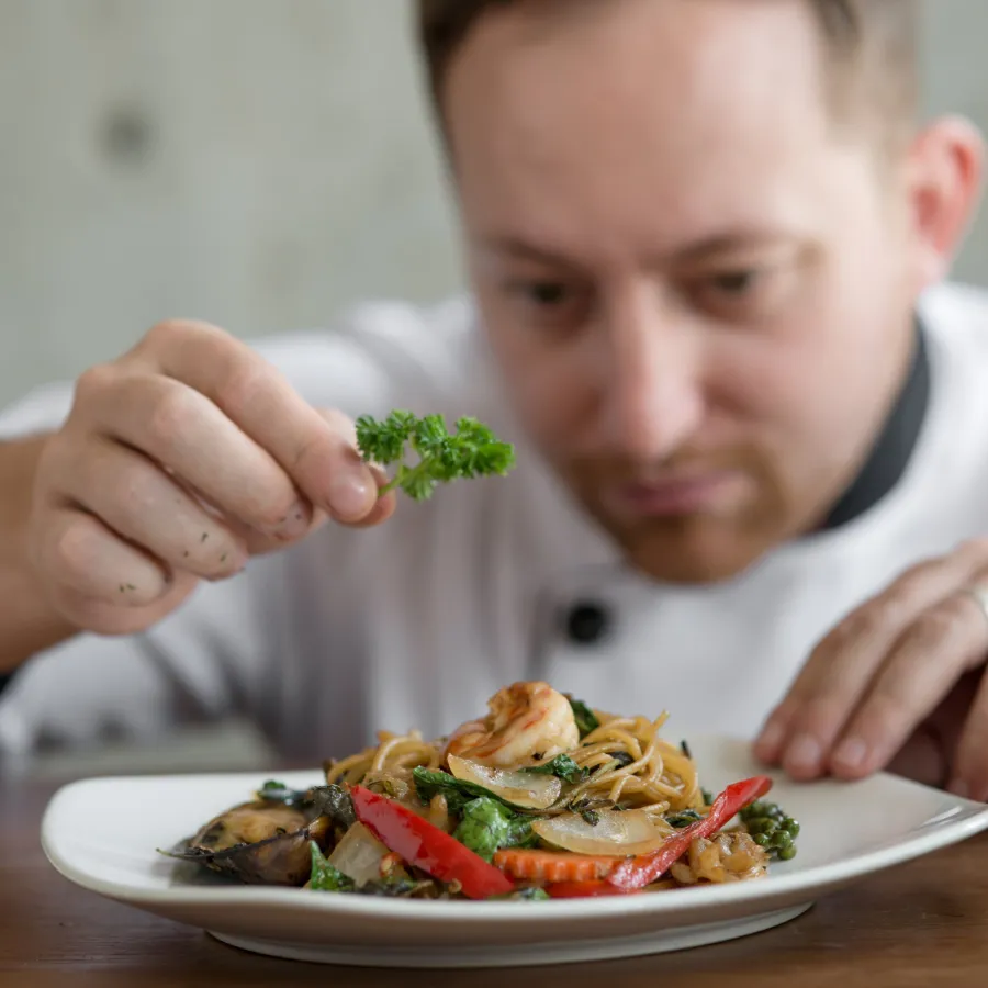 Gastronomie – Steuerberatung Düsseldorf Koch garniert ein Pastagericht mit Petersilie